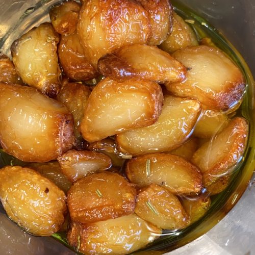 Dientes de ajo morado dorándose lentamente en una sartén con aceite de oliva.