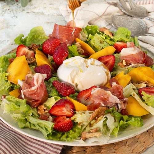 Ensalada fresca de verano con mango, fresas, burrata, jamón curado y lechuga miniromana Peregrín, servida como entrante saludable